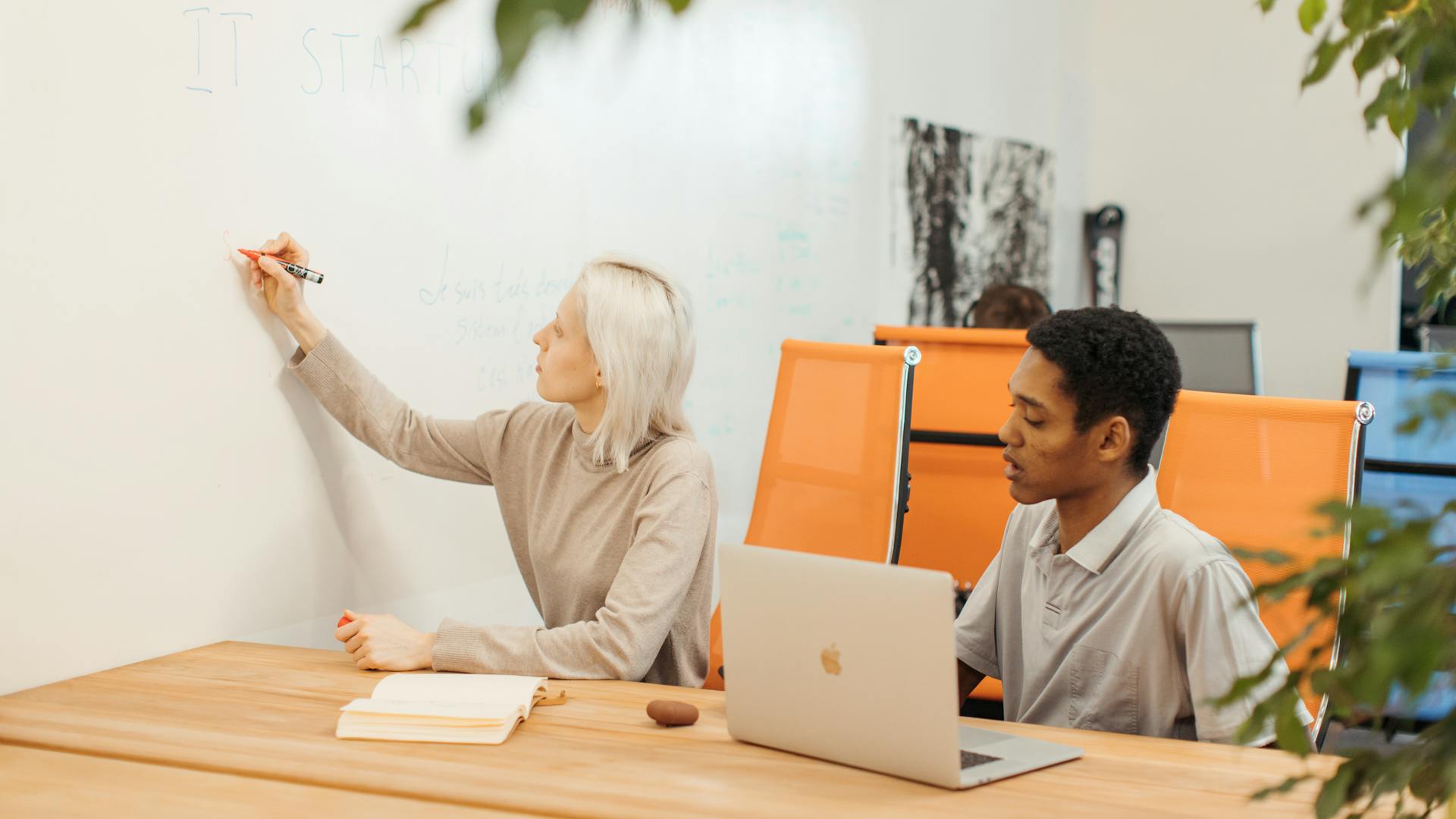 Two professionals collaborating at a startup office with a whiteboard and laptop.